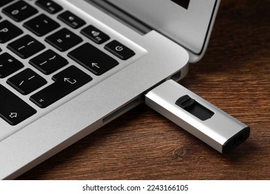 Usb flash drive attached into laptop on wooden table, closeup