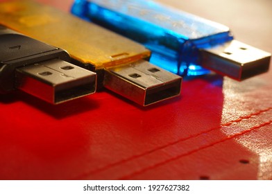 USB flash drive - black, yellow and blue, on a red background. Three used computer flash drives, ready to work. Close-up of a data memory stick, in several colors, on a bright background.