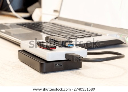 USB flash drives and external hard drives connected to a laptop on a desk for data storage and backup. Shortages and rising prices for storage devices