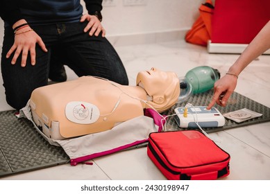 Use an automatic defibrillator in conducting basic cardiopulmonary resuscitation of victim. Automated external defibrillator device, AED with training dummy mannequin. Demonstrating chest compressions