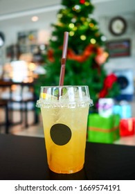 Use For Cafe,restaurant,food And Beverage Concept.Passionfruit Soda In Clear Plastic Cup With Brown Straw.Placed On Wooden Table.Christmas Tree As Background In Warm Mood Cafe.