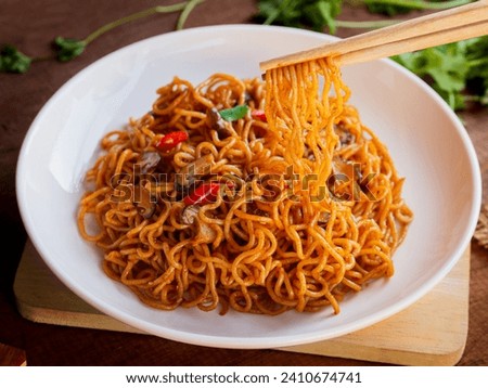Use chopsticks to pick up Instant noodles spicy with chicken, mushroom, white sesame, seaweed sheets and chili in white plate on wooden table background. Asia Food