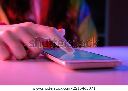 Use of mobile phone in trendy neon lights. Creative vivid color of ultraviolet red and blue. Hands of Teen Girl scrolling up photos Close-up at dark neon room. App for sale in shop. Social media.