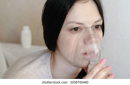 Use nebulizer and inhaler for the treatment. Closeup young woman's face inhaling through inhaler mask. Side view.
