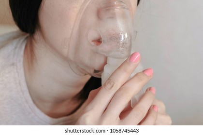 Use nebulizer and inhaler for the treatment. Closeup young woman's chin inhaling through inhaler mask. Side view.