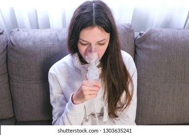 Use nebulizer and inhaler for the treatment. Young woman inhaling through inhaler mask sitting on the sofa.