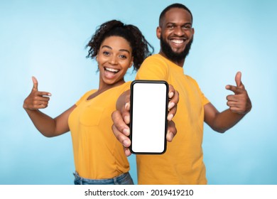 Use this new application. Cheerful black couple pointing at smartphone with blank screen, recommending mobile app, advertising your website, mockup for design. Selective focus - Shutterstock ID 2019419210