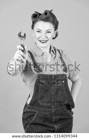 Use this tool! Attractive woman dressed in pin-up style with wrench in hand. Caucasian brunette model posing in retro fashion and vintage concept on grey background. Woman and wrench.