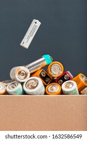 Used Battery Falling Into A Cardboard Box Filled With Discharged Batteries. Waste Disposal And Recycling. Front View With Copy Space For Text