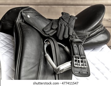 Used Black Dressage Horse Riding Saddle With Girth, Stirrup And Riding Gloves On White Saddle Pad