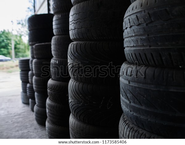 Used car tires stacked in piles at\
junkyard. Old wheels recycling and utilization\
concepr