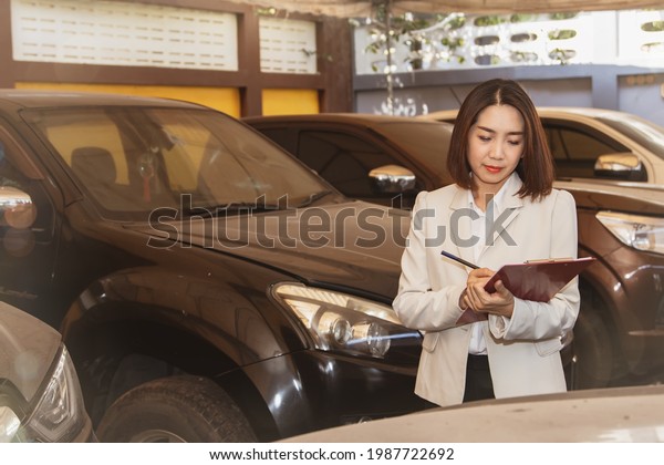 Used car trade\
concept : Asian businesswoman or a used car dealer checks vehicle\
records and the number of cars parked in garages with pickup trucks\
popular with the\
recession.