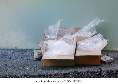 Used Cardboard Box With Plastic Air Bubble Wrapped Pile Messily Beside Cement Wall, Waiting To Be Collected Or Reused.