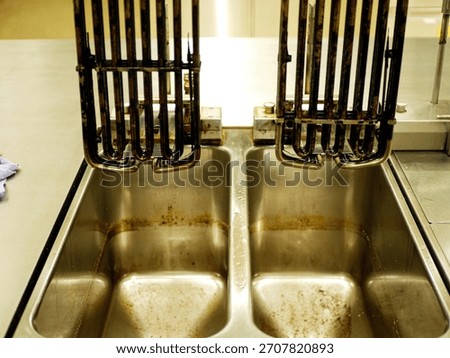 Used deep fryer heating elements placed above stainless steel basins with oil residue in professional restaurant kitchen after frying and before cleaning. High quality photo. 