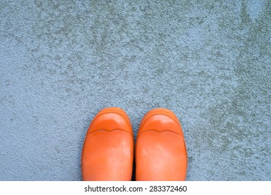 Used, Dirty, Orange Rubber Wellington Boots On A Grungy Concrete Surface With Lots Of Copy Space, Top View, Horizontal