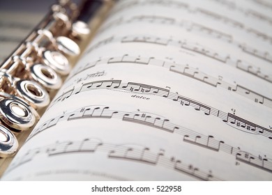 A used flute lies along the spine of an open musical score. Only one line of music is in focus.