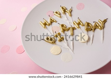Used Happy Birthday candle letters on a party plate surrounded by confetti. Selective focus