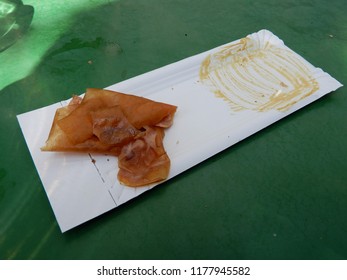 A Used Paper Plate With A Rest Of The Sausage And The Bread With Mustard