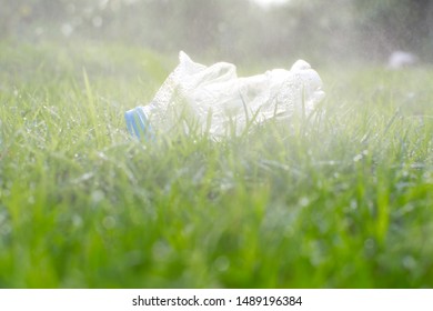 The Used Plastic Bottle On Green Grass  Over Green Nature Background In Rainy Time. The Conceptual Concept Of Save The Earth By To End Plastic Waste Pollution. Copy Space For Text On Top.