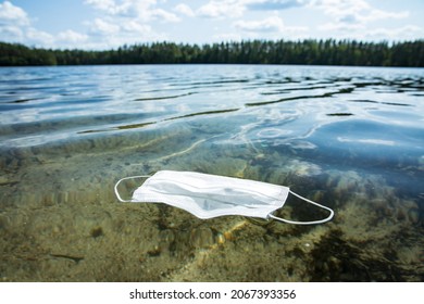 Used protection mask floating in clear water. Global environmental problem of pollution after COVID-19 pandemic on planet. Waste in ocean. 