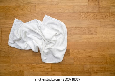 Used white towel lying on wooden floor at a hotel room