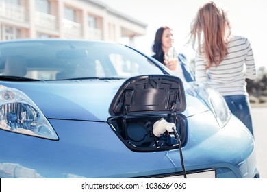 Useful nowadays. Blue comfortable electric car staying near girls and charging.