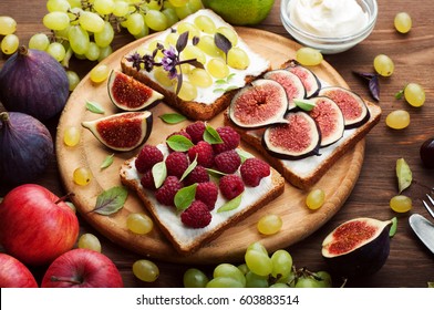 Useful organic sandwiches with diet cheese cream, raspberries, green grapes and figs on a round wooden cutting board. Next to apples, grapes and figs. Selective sharpness. Close-up - Shutterstock ID 603883514