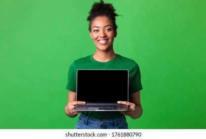 Useful Website. Cheerful afro girl holding laptop computer, showing blank screen over green studio wall, mock up