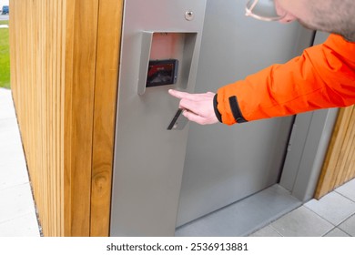 user enters PIN while wearing orange jacket, hand in orange jacket presses button, User interacts with electronic panel, outdoor public toilet, Berlin - February 17, 2024 - Powered by Shutterstock