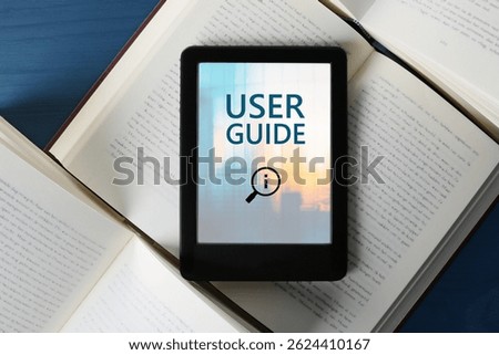 User Guide document open in e-book device and different books on blue wooden table, top view