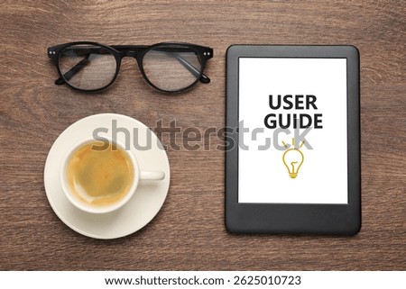 User Guide document open in e-book device, cup of coffee and eyeglasses on wooden table, flat lay