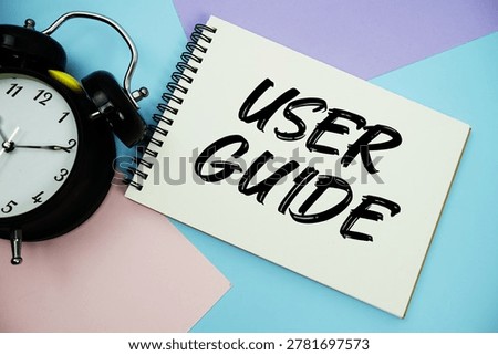 User Guide text written on notepad with alarm clock flat lay on multicolor pastel background