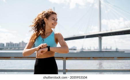 Uses a smart watch to measure the pulse on the hands. A woman does sports on the street. Fitness and a healthy lifestyle. The trainer does exercises for stretching the body. - Powered by Shutterstock