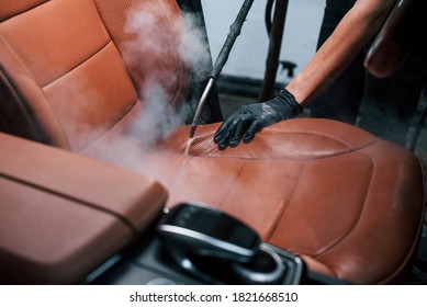 Uses steam cleaner. Modern black automobile is in service by woman inside of car wash station.