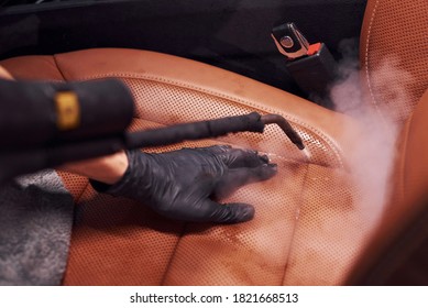 Uses Steam Cleaner. Modern Black Automobile Is In Service By Woman Inside Of Car Wash Station.