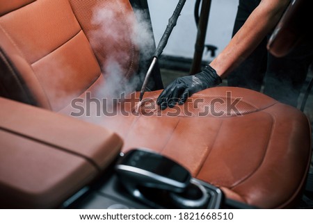 Uses steam cleaner. Modern black automobile is in service by woman inside of car wash station.