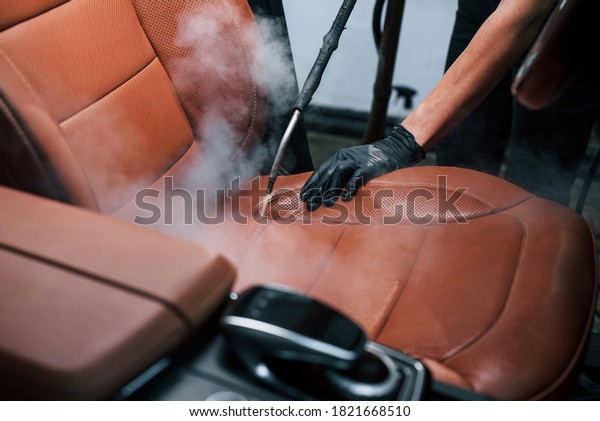 Uses steam cleaner. Modern\
black automobile is in service by woman inside of car wash\
station.