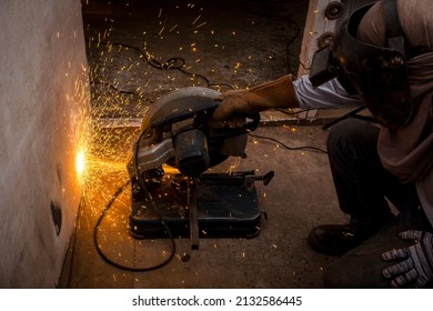 Using A Abrasive Cutoff Machine Or Chop Saw On The Floor To Cut A Piece Of Steel Square Tube. Action Shot With Sparks Flying At A Furniture Workshop.