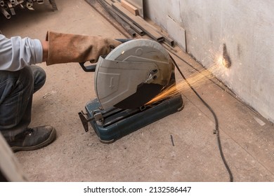 Using A Abrasive Cutoff Machine Or Chop Saw On The Floor To Cut A Piece Of Steel Square Tube. Action Shot With Sparks Flying At A Furniture Workshop.