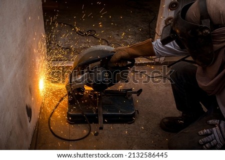 Using a Abrasive Cutoff Machine or chop saw on the floor to cut a piece of steel square tube. Action shot with sparks flying at a furniture workshop.
