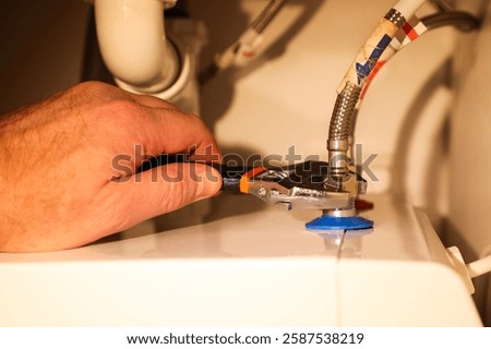 Using an adjustable wrench, a professional plumber connects hot and cold water hoses to a boiler.