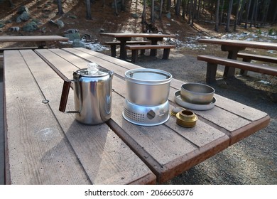 Using An Alcohol Camping Stove In The Woods. Percolator, Cooking Pot, Fuel Container, Handle, Picnic Table.