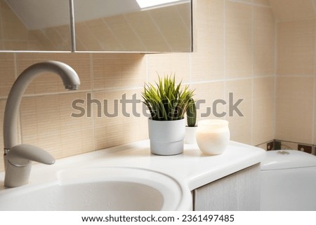 Using artificial flowers in bathroom interior at home. Potted flower plant on bathroom sink corner with candle burning.