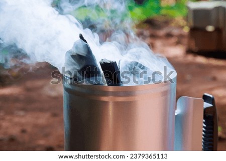 Using barbecue chimney starter to get charcoal ready for cooking on grill, which is glowing hot