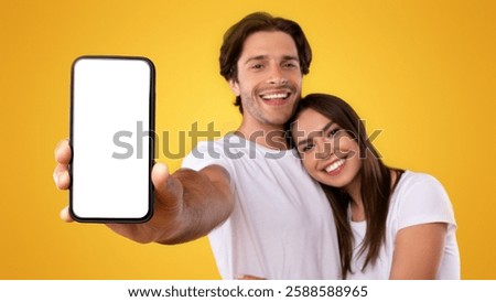 Using Cool Application. Portrait of cute millennial couple holding smartphone with white screen in hand, recommending mobile app, advertising your website, hugging, mock up for design. Selective focus
