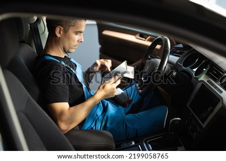 Using digital tablet for car diagnostic. Interactive diagnostics software on an advanced computer. Mechanic using tablet pc at the repair garage service.