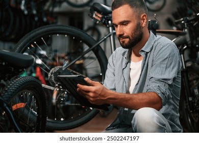 Using digital tablet. Repair man in bicycle shop, working in store. - Powered by Shutterstock