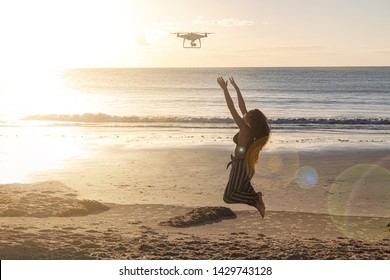 Using a drone uses remote control on the beach. Full length shot of young woman operating the drone by remote control at the sea shore. Brazil.