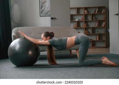Using fitness ball. Young woman in yoga clothes doing fitness indoors.