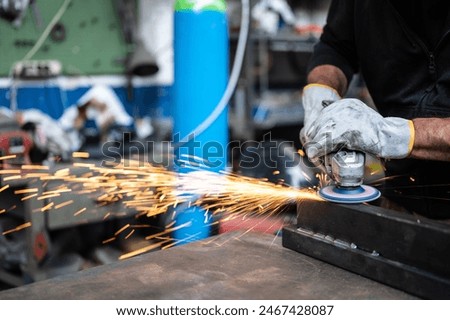 Using the flexible disc grinder on a metal bar: When the tool touches the surface, numerous orange sparks are projected. Concept of metal processing in the workshop. Craft work, metal working.